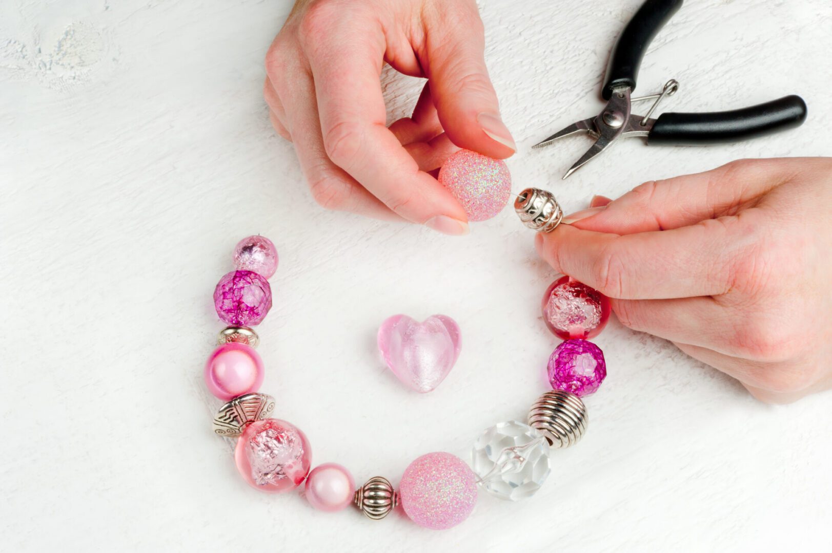 Hands assembling pink beaded necklace